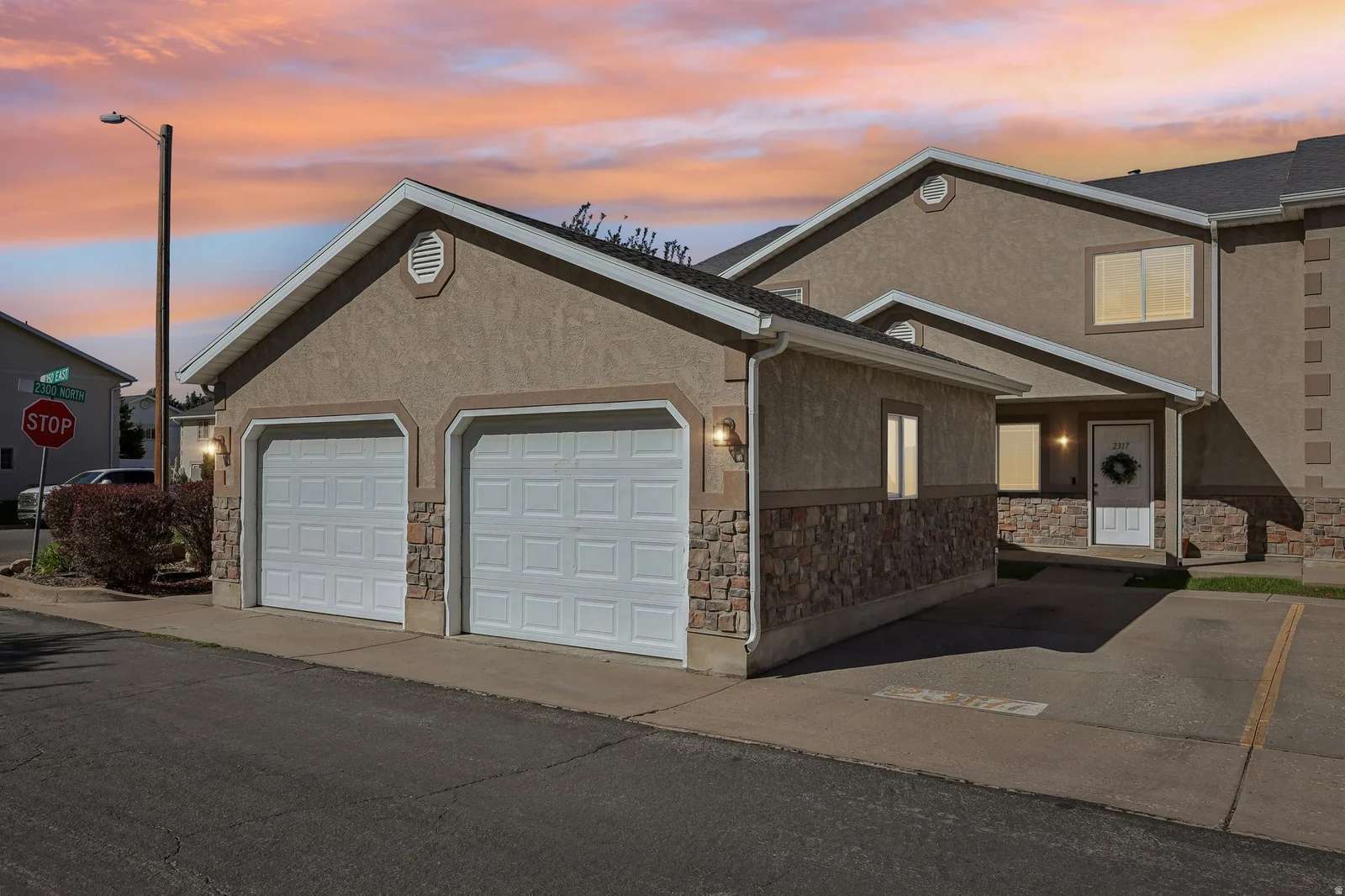 Stucco exterior with stone veneer accents, white panel garage doors, and a covered entry
